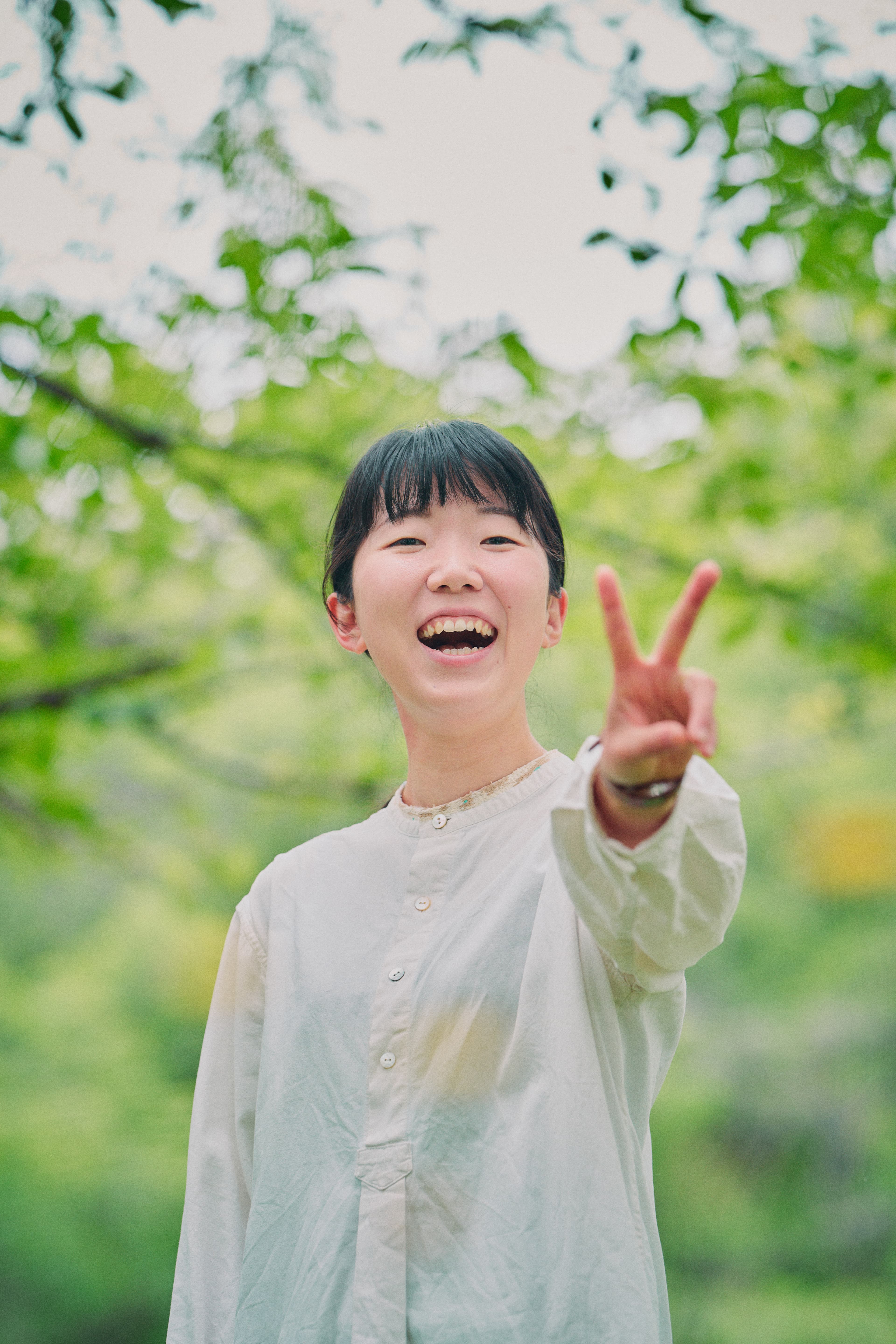 緑の中で笑いながらピースする人物