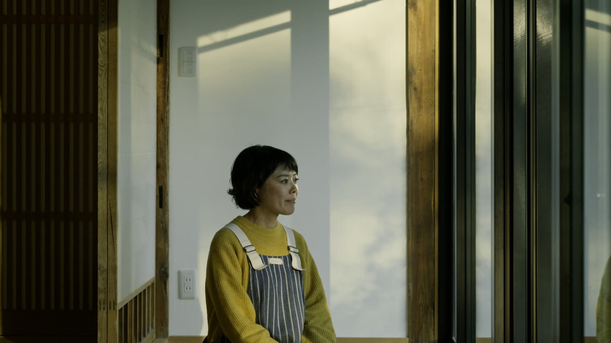 窓からの光を受けて立つエプロン姿の女性